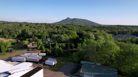 aerial-low-flight-toward-pilot-mountain-nc,-north-carolina-with-forest-in-the-foreground-and-mountain-in-the-background,-the-pinnacle-in-the-background