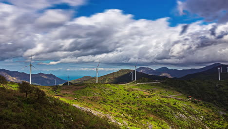 View-of-rows-of-white-wind-mills-over-a-hilly-terrain-with-green-vegetation-with-white-clouds-passing-by-on-a-cloudy-day