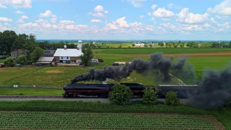 Eine-Parallele-Luftaufnahme-Eines-Antiken-Dampfzugs,-Der-An-Einem-Sonnigen-Tag-Mit-Schwarzem-Rauch-Durch-Ackerland-Fährt