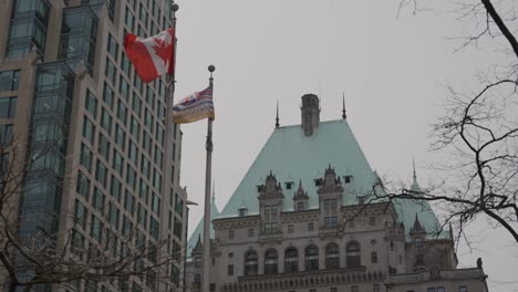 Close-up-of-Canada-and-British-Columbia-flags-waving-in-front-of-Fairmont-Hotel-copper-rooftop-in-Downtown-Vancouver