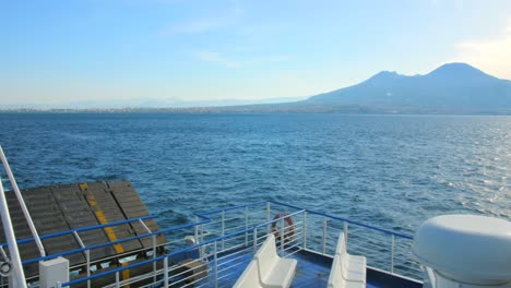 Italian-flag-blowing-in-the-wind-on-boat-ride-across-Mediterranean-Sea-with-Mount-Vesuvius-on-the-side-leaving-Naples,-Italy