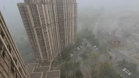 Fantastic-powerful-wild-nature-wind-and-rain-storm-point-of-view,-looking-out-of-window-from-high-rise-building-overlooking-at-hailing-weather-with-hailstones-falling-and-foggy-atmosphere