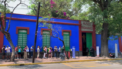 Tilt-Down-From-Trees-To-Reveal-Visitors-Queuing-Outside-The-Famous-Blue-House-Of-Frida-Kahlo-Museum