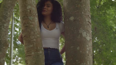 Sexy-latina-woman-standing-in-the-middle-of-two-tree-trunk-while-smiling