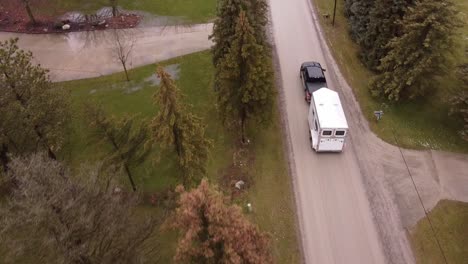 Black-pick-up-truck-towing-horse-trailer-through-small-town,-aerial-follow-view