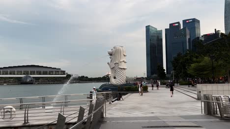 Tourists-visiting-and-locals-exercise-at-merlion-park-at-downtown-metropolitan-area-with-business-and-financial-buildings-in-the-background