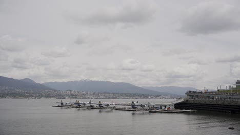 Seaplanes-docked-inline-in-Vancouver-Harbour-Flight-Centre,-sea-bay-and-mountains-in-background,-British-Columbia,-Canada