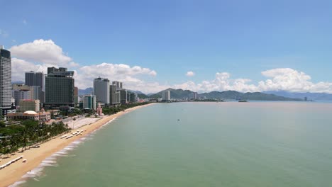 low-altitude-aerial-view-of-the-Nha-Trang-coastline-full-of-white-beach-umbrellas-on-a-sunny-day-with-tall-hotels-overlooking-the-palm-trees-and-turquoise-water