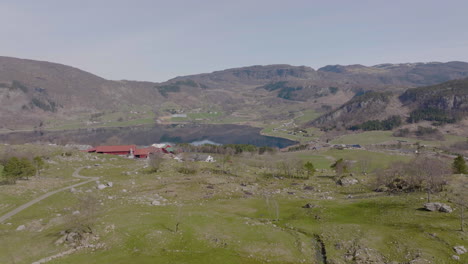 Norwegian-aerial-landscape-of-farmhouse-and-farmers-land,-lake-and-mountain-scenery
