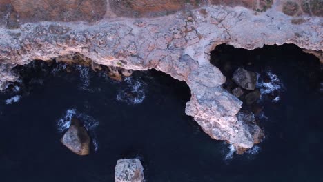 Top-down-aerial-view-of-waves-splash-against-rocky-seashore,-background