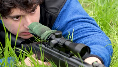 Male-lying-on-the-grass,-aiming-through-his-weapon-sight