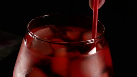 Stirring-red-refreshing-icy-drink-with-straw,-black-bacground,-isolated-close-up