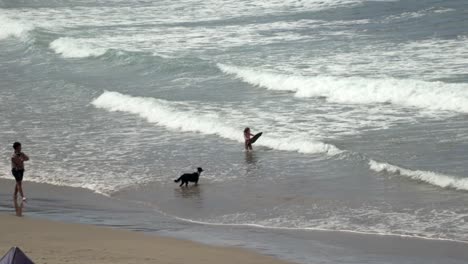 Kleines-Kind-Im-Meer-Mit-Einem-Bodyboard-Und-Seinem-Schwarzen-Hund-Am-Strand
