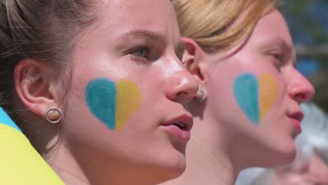 Protesters-are-seen-with-their-faces-painted-with-a-heart-shape-in-blue-and-yellow-colors,-the-Ukraine-flag-colors,-during-a-rally-against-the-Russian-invasion-of-Ukraine-in-Spain