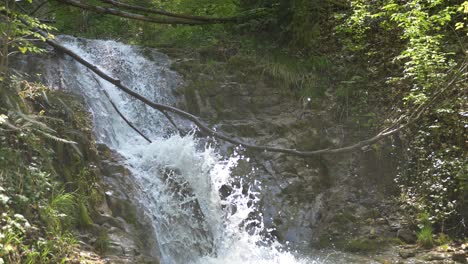 Close-up-shot-of-water-falling-down-mountain-waterfall-in-tree-jungle-during-sunny-day---slow-motion