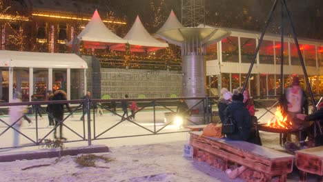 Many-people-skating-on-colorful-ice-skating-rink-at-night-with-warming-up-next-to-campfire-during-winter-in-Oslo,-Norway