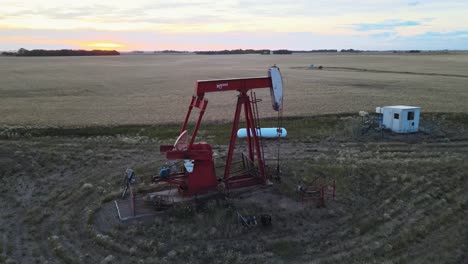Wide-angle-drone-shot-of-an-active-red-pumpjack-in-the-countryside-of-north-America-at-sunset