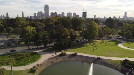 Fountain-on-lake-in-Tres-de-Febrero-park-with-skyscrapers-in-background,-Buenos-Aires-city