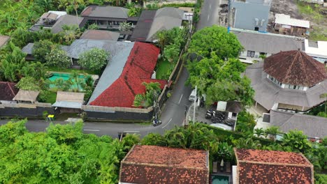 motorbikes-driving-around-a-bend-in-local-balinese-neighborhood-of-Umalas,-aerial