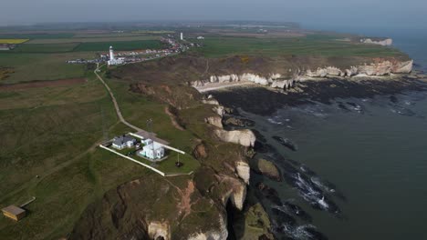 Aerial-view-following-Yorkshire-white-coastline-cliffs-above-scenic-green-landscape-towards-Flamborough-Head-Lighthouse