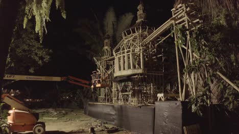 Performance-stage-temple-of-the-Envision-Festival-being-set-up-at-night-with-a-crane,-Aerial-closing-in-shot