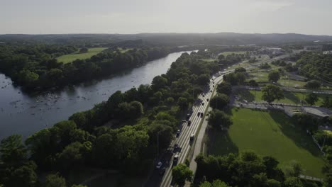 Aerial-view-of-traffic-on-the-Cesar-Chavez-street,-revealing-paddlers-on-the-Colorado-river,-in-sunny-Austin,-USA---pan,-drone-shot