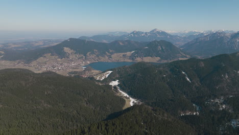 Scenic-Aerial-5K-Drone-Over-German-Alps-Mountaintop-With-Forest,-Snowy-Valley-And-Lake-Views