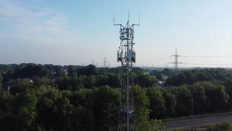 5G-broadcasting-tower-mast-in-British-countryside-with-vehicles-travelling-on-highway-background-aerial-left-orbit-view