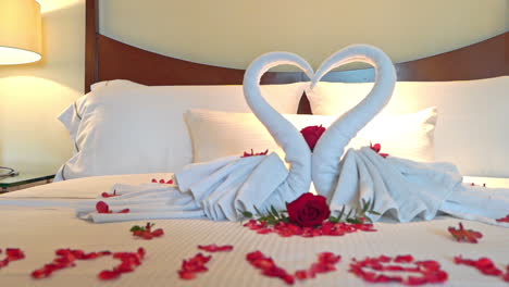 Hotelzimmer-Mit-Frischen-Handtüchern-Als-Herzsymbol-Oder-Zwei-Schwänen,-Auf-Den-Weißen-Laken-Das-Wort-„Jubiläum“-Mit-Roten-Rosenblättern-Eingelegt