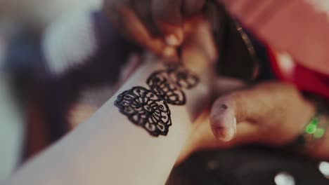Primer-Plano-Artista-De-Henna-Aplica-Un-Tatuaje-De-Henna-En-El-Brazo-De-La-Mujer