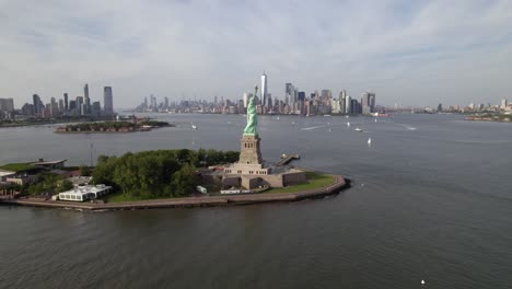 Aerial-view-passing-the-Statue-of-Liberty,-towards-the-Lower-Manhattan-skyline,-in-NYC,-USA