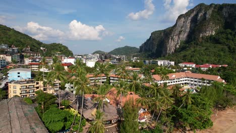 aerial-drone-flying-overhead-large-coconut-palm-trees-revealing-the-town-of-Ao-Nang-in-Krabi-Thailand-on-a-sunny-summer-day-with-large-limestone-mountain-cliffs-in-the-distance