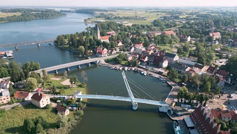 Mikolajki,-Poland---Descend-aerial-bird-drone-view-flight-over-the-pedestrian-bridge-most-wiszacy-of-the-touristic-city-in-Warmian-Masurian-with-blue-sea-and-tiny-ships-and-yachts-in-summer-2022