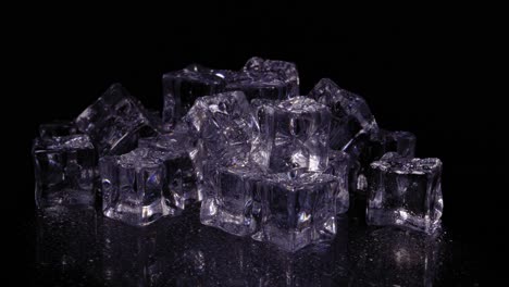 Pile-of-ice-cubes-with-a-purple-tint-rotating-against-a-black-background,-downward-static-studio-shot