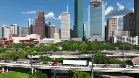 Aerial-reveal-of-downtown-Houston-Texas-skyline-as-traffic-rushes-by-on-interstate-freeway-highways