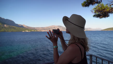 Female-Tourist-Taking-Photos-Of-A-Majestic-Mountain-Range-Surrounded-With-Turquoise-Island-Water