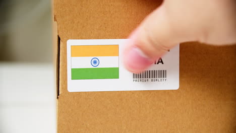 Manos-Aplicando-La-Etiqueta-De-La-Bandera-De-India-En-Una-Caja-De-Cartón-De-Envío-Con-Productos