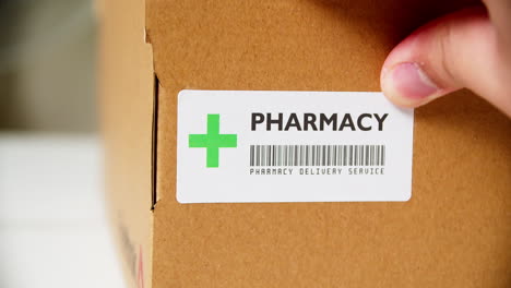 Manos-Aplicando-La-Etiqueta-Adhesiva-De-La-Farmacia-En-Una-Caja-De-Cartón-De-Envío