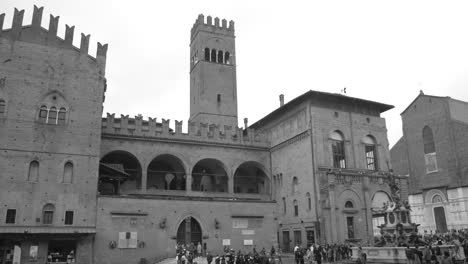 Black-and-white-shot-of-tourists-crowding-around-Palazzo-del-Podesta-in-Bologna,-Italy-at-daytime