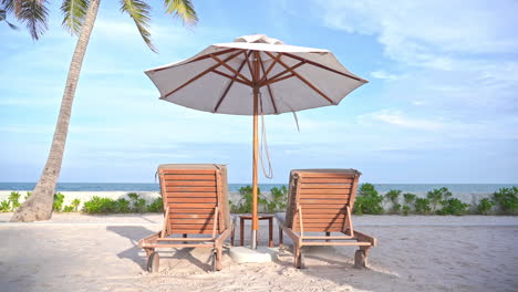 A-pair-of-empty-beach-loungers-under-a-shade-umbrella-point-out-to-an-ocean-view