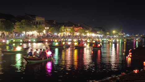 Timelapse-Hoi-An-Lantern-Festival,-Colorful-Lantern-Lit-Nights-Celebration,-Lots-of-Boats-Canoes-Traffic-on-the-Canal-River-Floating-Sailing-Along-the-Quay,-Tourists-Crowd,-Glowing-Lanterns-on-Water