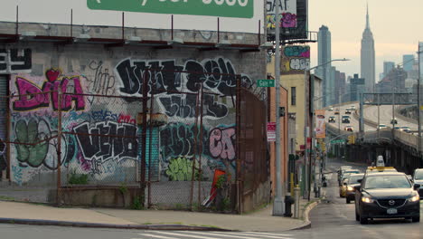 Stark-Mit-Graffiti-Versehenes-Gebäude-In-Queens,-New-York,-Mit-Dem-Empire-State-Building-Im-Hintergrund