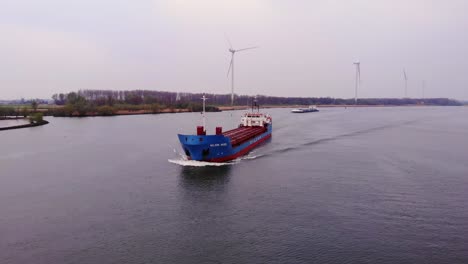 Aerial-View-Of-Wilson-Mosel-Cargo-Ship-Approaching-Along-Oude-Maas-With-Still-Wind-Turbines-In-Background-In-Barendrecht