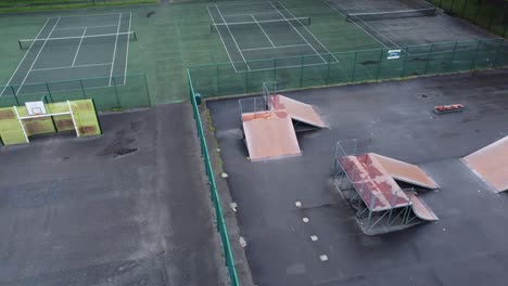 Aerial-view-Birdseye-descent-flying-above-fenced-skate-park-ramp-in-empty-closed-playground