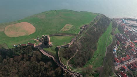 Aerial-view-above-Scarborough-castle-hillside-landmark-overlooking-beautiful-English-harbour-townscape-coastline