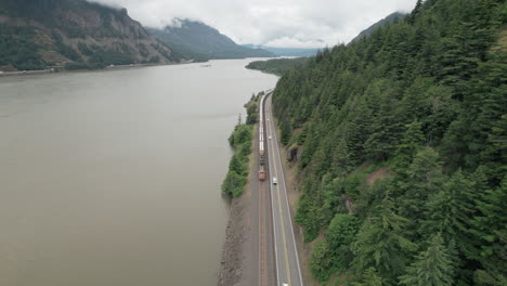 Freight-train,-traffic-along-Columbia-River-travels-towards-camera,-reverse-aerial-dolly