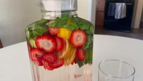 Healthy-Drinks-in-the-Kitchen,-Push-in-Shot-of-Fruit-Infused-Spa-Water-on-White-Table
