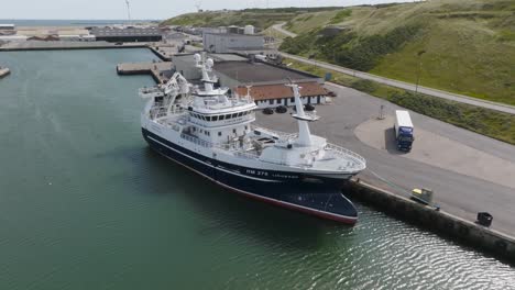In-this-aerial-view,-the-white-and-blue-colored-fishing-trawler-Linkbank-is-moored-in-the-port-near-the-pier-in-Hanstholm,-Denmark