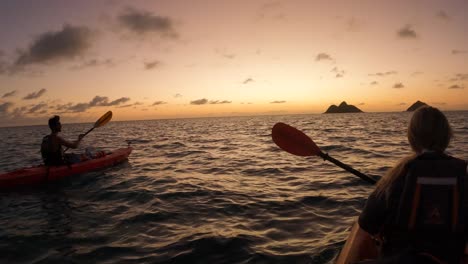Couple-paddling-kayaks-on-sea-towards-sunset-horizon,-slow-motion