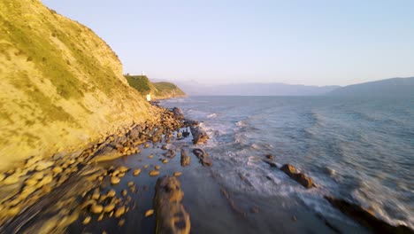 Drone-low-to-high-flight-along-rocky-coast-of-Vlore,-small-waves-washing-on-beach,-Albania